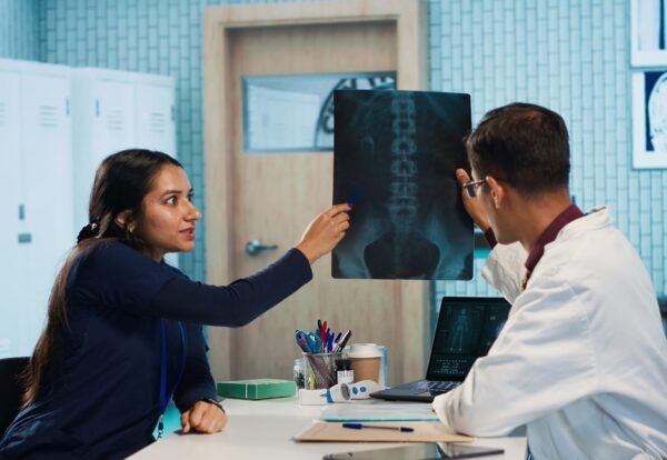 Indian general practitioner and nurse examine hospital records and x ray tests, finding diagnosis for a patient. Medical staff reviewing scans and doing healthcare reports with expertise. Camera A.