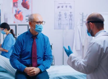 Senior man at doctor appointment during COVID-19 pandemic. Patient wearing mask and doctor in protective wear. Healthcare consultation, medicinal system. Private modern clinic